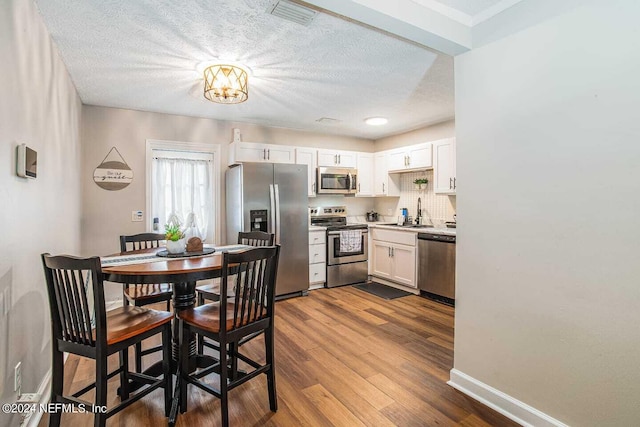 dining area with an inviting chandelier, a textured ceiling, sink, and light hardwood / wood-style floors