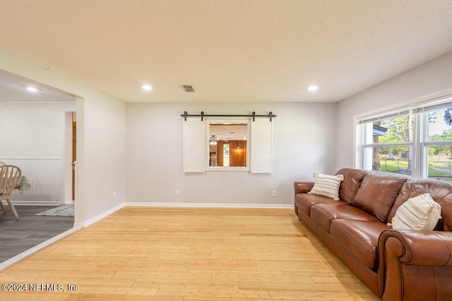 living room featuring a barn door, light hardwood / wood-style floors, and a textured ceiling