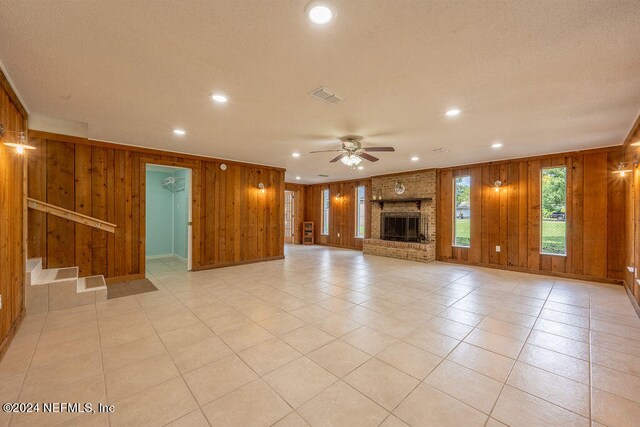 unfurnished living room with a brick fireplace, wood walls, light tile patterned floors, and ceiling fan