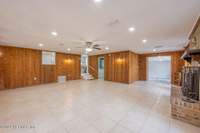 unfurnished living room with wooden walls, ceiling fan, and a fireplace