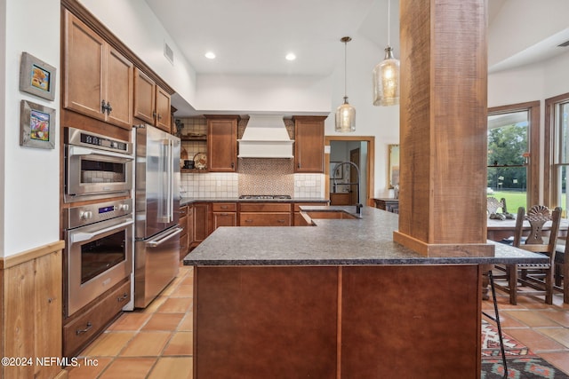 kitchen featuring a breakfast bar area, sink, hanging light fixtures, appliances with stainless steel finishes, and premium range hood