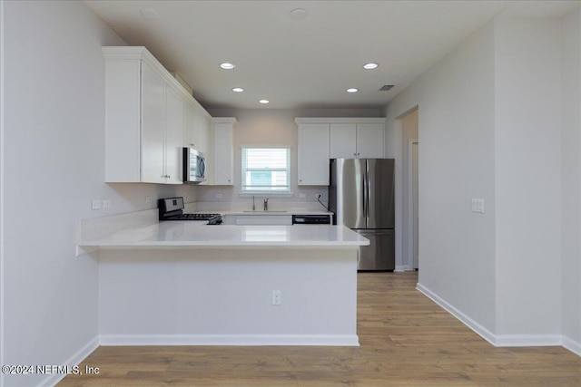 kitchen with light hardwood / wood-style flooring, stainless steel appliances, kitchen peninsula, and white cabinetry