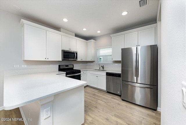 kitchen featuring light wood-type flooring, sink, white cabinets, kitchen peninsula, and appliances with stainless steel finishes