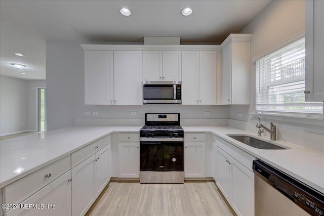 kitchen with light hardwood / wood-style floors, sink, white cabinets, stainless steel appliances, and light stone countertops