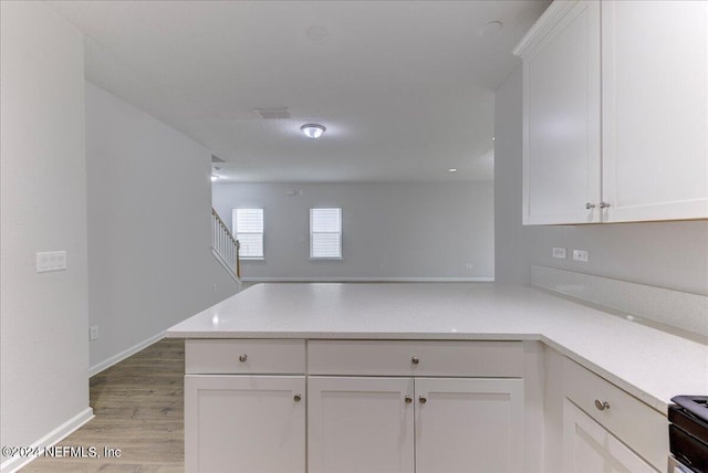 kitchen with white cabinets, light hardwood / wood-style flooring, stainless steel electric range oven, and kitchen peninsula