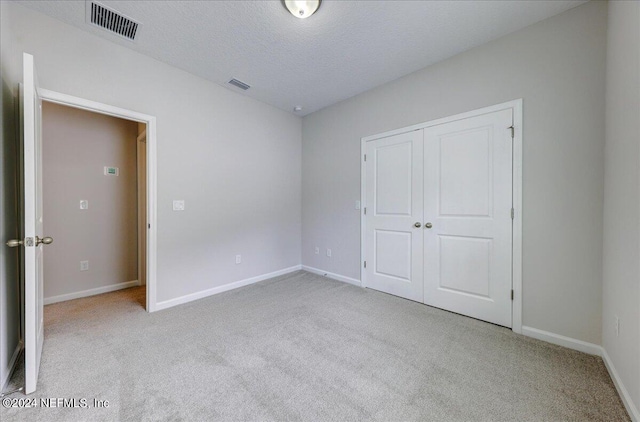 unfurnished bedroom with light carpet, a textured ceiling, and a closet