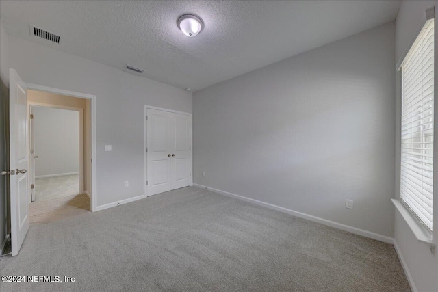 unfurnished bedroom with light colored carpet, a textured ceiling, and a closet