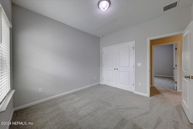 unfurnished bedroom with light carpet, a closet, and a textured ceiling