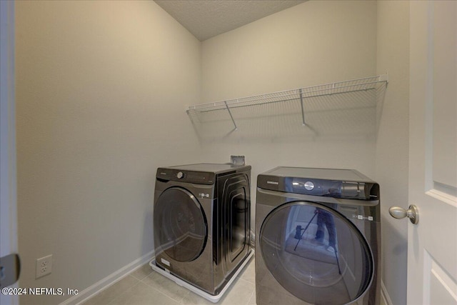 clothes washing area featuring a textured ceiling, light tile patterned floors, and washing machine and clothes dryer