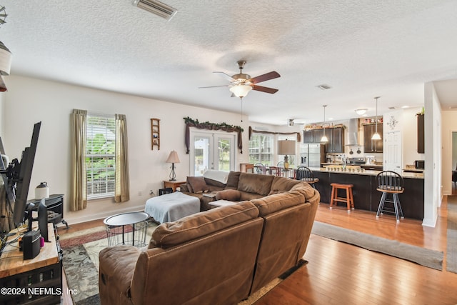 living room featuring ceiling fan, a healthy amount of sunlight, a textured ceiling, and light hardwood / wood-style flooring