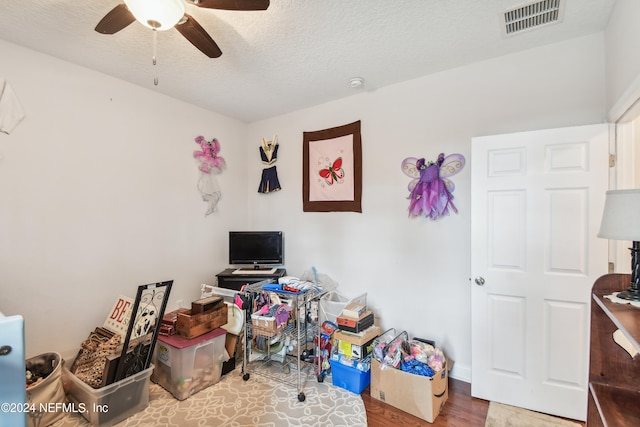 game room featuring wood-type flooring, a textured ceiling, and ceiling fan