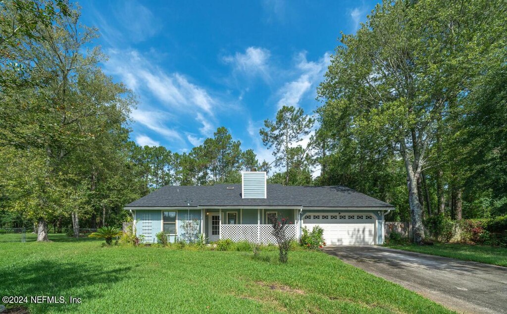 ranch-style home featuring a chimney, concrete driveway, a garage, and a front lawn
