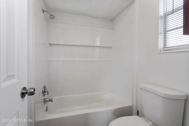 bathroom with a textured ceiling, tiled shower / bath combo, and toilet