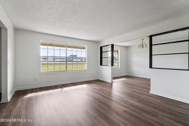 empty room featuring a textured ceiling, dark wood-type flooring, and a notable chandelier