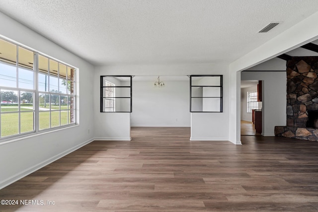 unfurnished living room featuring a stone fireplace, a textured ceiling, and dark hardwood / wood-style flooring