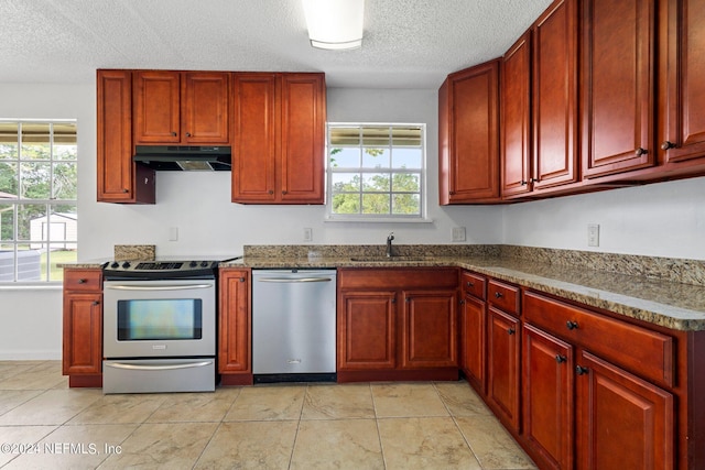 kitchen featuring reddish brown cabinets, under cabinet range hood, a wealth of natural light, and appliances with stainless steel finishes