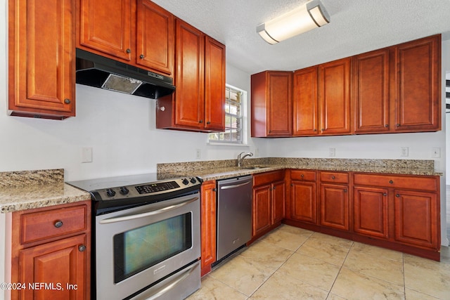 kitchen featuring light stone counters, a sink, appliances with stainless steel finishes, a textured ceiling, and under cabinet range hood