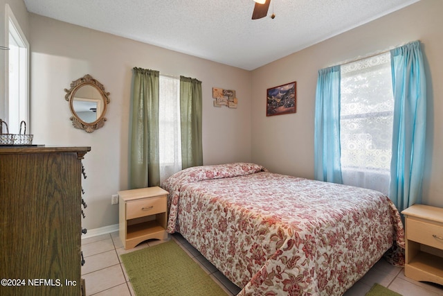 bedroom featuring light tile patterned flooring, a textured ceiling, baseboards, and a ceiling fan