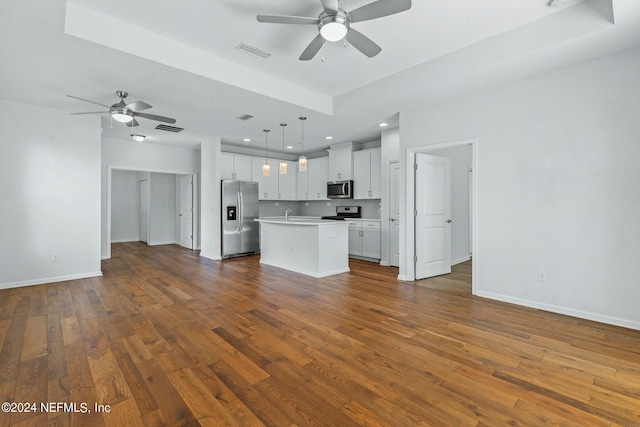 unfurnished living room with a tray ceiling, ceiling fan, and dark wood-type flooring