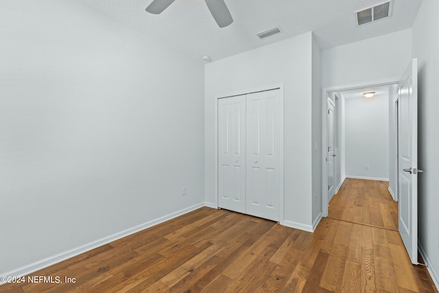 unfurnished bedroom featuring wood-type flooring, a textured ceiling, a closet, and ceiling fan