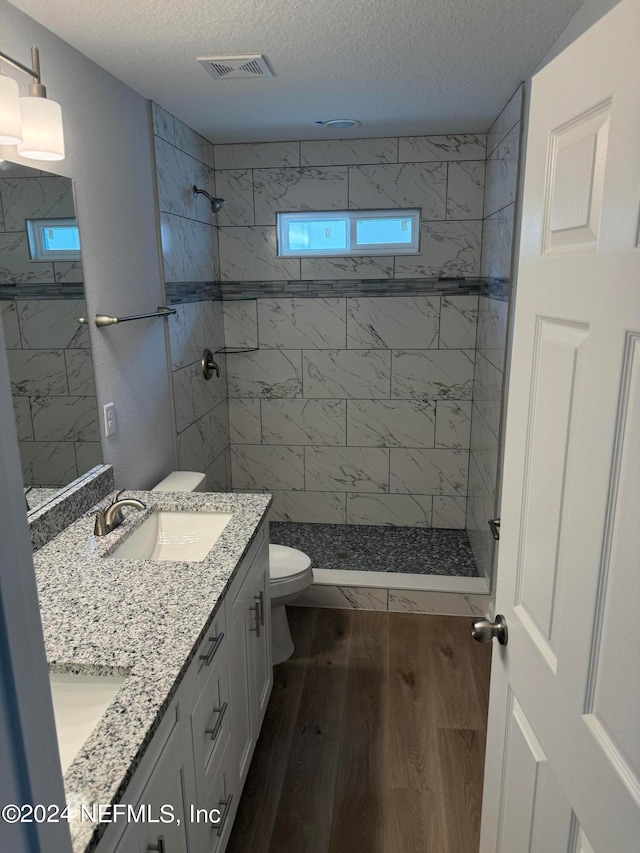 bathroom with a tile shower, hardwood / wood-style flooring, vanity, and toilet