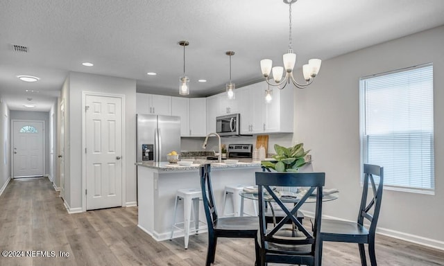 kitchen with pendant lighting, light hardwood / wood-style floors, white cabinets, a kitchen breakfast bar, and stainless steel appliances