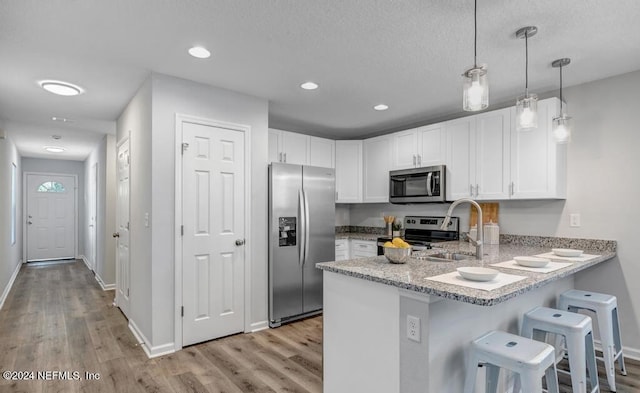 kitchen featuring sink, white cabinets, kitchen peninsula, hanging light fixtures, and stainless steel appliances