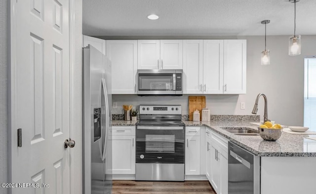 kitchen with light stone countertops, white cabinets, appliances with stainless steel finishes, and hanging light fixtures