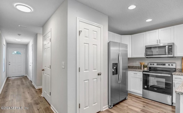 kitchen featuring light stone countertops, stainless steel appliances, white cabinets, and light wood-type flooring