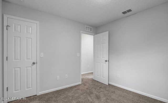 unfurnished room featuring a textured ceiling and light carpet