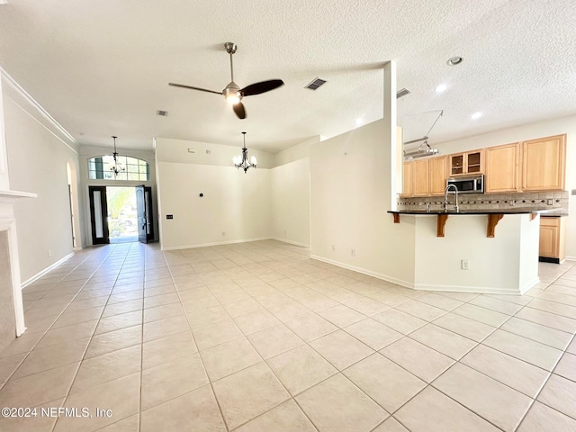 unfurnished living room with a textured ceiling, sink, light tile patterned floors, and ceiling fan with notable chandelier