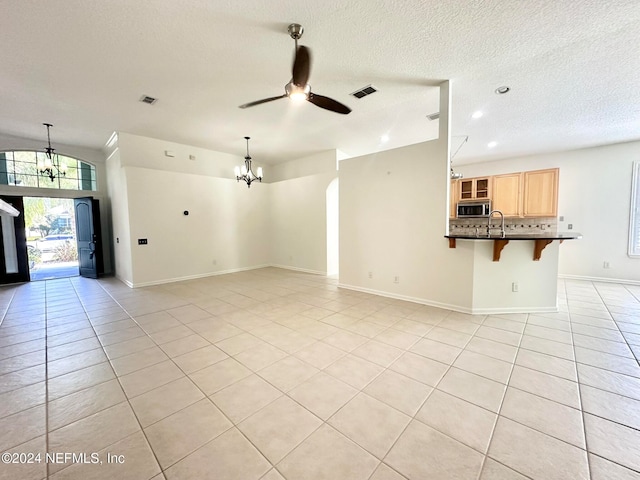 unfurnished living room with a textured ceiling, sink, light tile patterned floors, and ceiling fan with notable chandelier