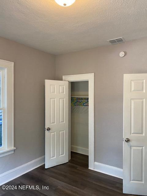 unfurnished bedroom featuring a textured ceiling, a closet, and dark hardwood / wood-style flooring