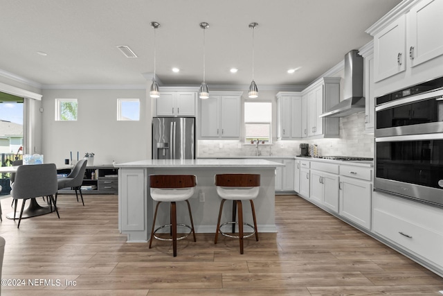 kitchen featuring a center island, white cabinetry, wall chimney exhaust hood, appliances with stainless steel finishes, and decorative light fixtures