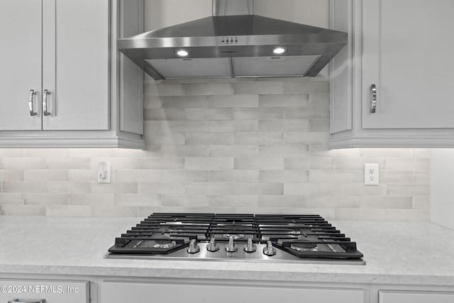 kitchen with backsplash, wall chimney exhaust hood, stainless steel gas cooktop, and white cabinetry