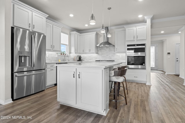 kitchen featuring white cabinets, a center island, appliances with stainless steel finishes, and wall chimney range hood