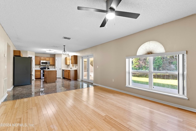 unfurnished living room with light hardwood / wood-style floors, a textured ceiling, ceiling fan, french doors, and sink