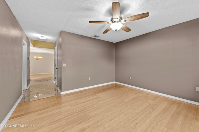 spare room featuring a textured ceiling, ceiling fan with notable chandelier, and hardwood / wood-style flooring