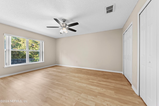 unfurnished bedroom featuring ceiling fan, a textured ceiling, light wood-type flooring, and two closets