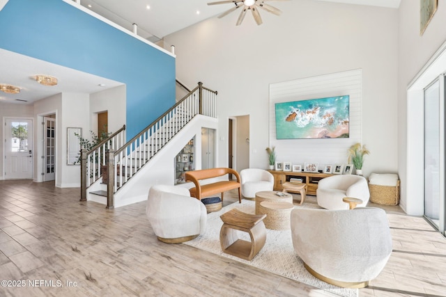 living room with ceiling fan, stairway, a high ceiling, and wood finished floors