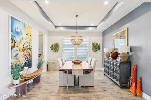 dining room with a notable chandelier, recessed lighting, a raised ceiling, wood finished floors, and baseboards