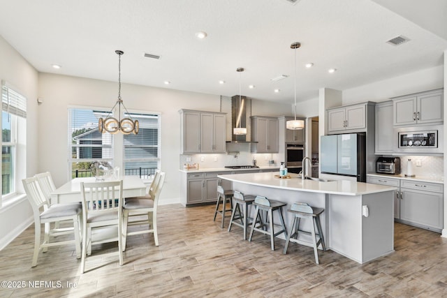 kitchen with stainless steel appliances, gray cabinets, wall chimney range hood, and tasteful backsplash