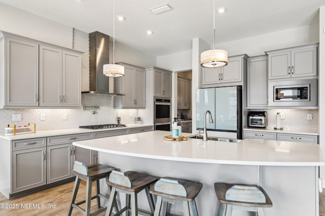 kitchen featuring stainless steel appliances, wall chimney range hood, gray cabinets, and light countertops