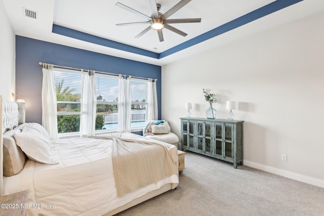 bedroom with carpet floors, visible vents, a tray ceiling, and baseboards