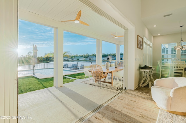 sunroom / solarium with a water view, visible vents, and ceiling fan with notable chandelier