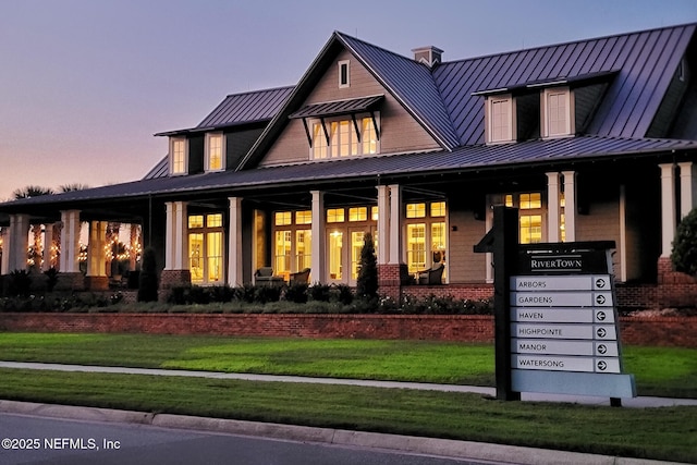 back of house at dusk with a porch, a standing seam roof, a lawn, and metal roof