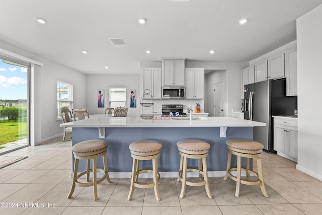 kitchen with white cabinets, light tile patterned floors, a kitchen island with sink, appliances with stainless steel finishes, and a breakfast bar