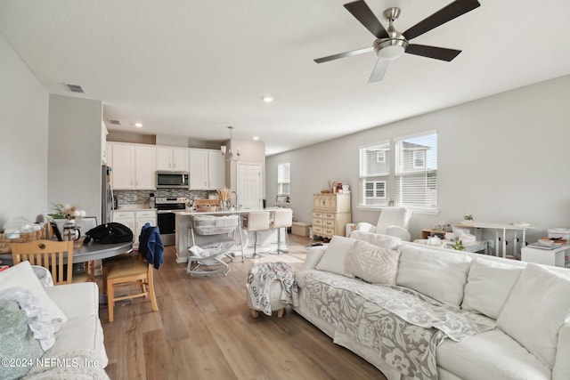 living room with ceiling fan with notable chandelier and light hardwood / wood-style floors