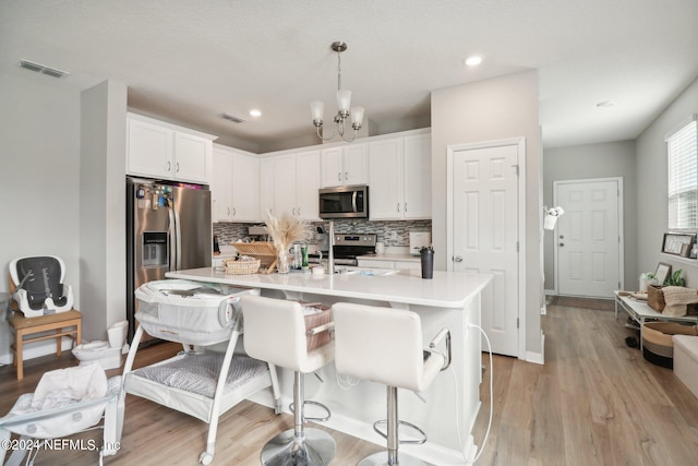 kitchen with light wood-type flooring, a breakfast bar area, white cabinetry, hanging light fixtures, and stainless steel appliances