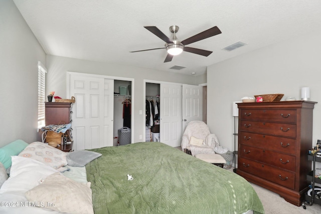 bedroom with light carpet, multiple closets, and ceiling fan